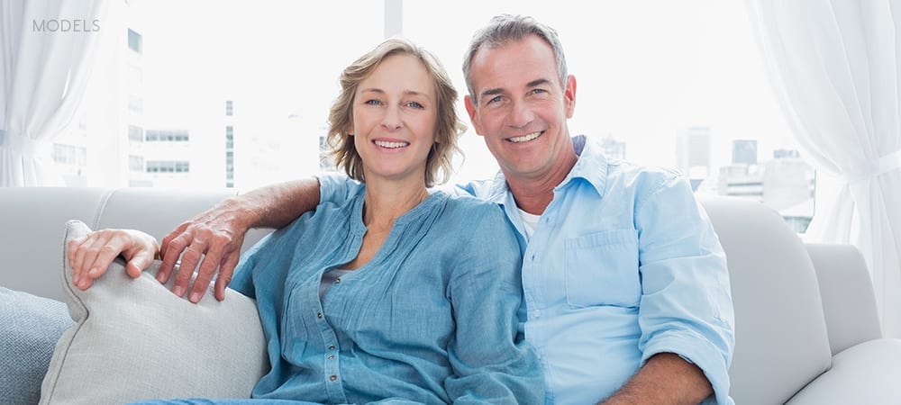Mature Caucasian Couple In Blue Shirts Embracing on Gray Couch